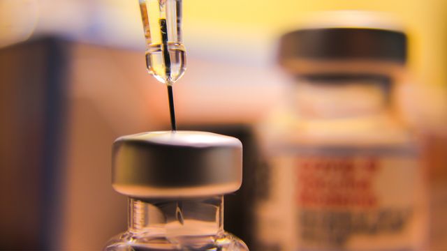 A close up of a syringe drawing liquid from a vaccine vial. 