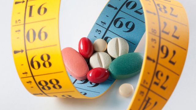 A selection of different drugs on top of a yellow tape measure used for measuring weight loss. 
