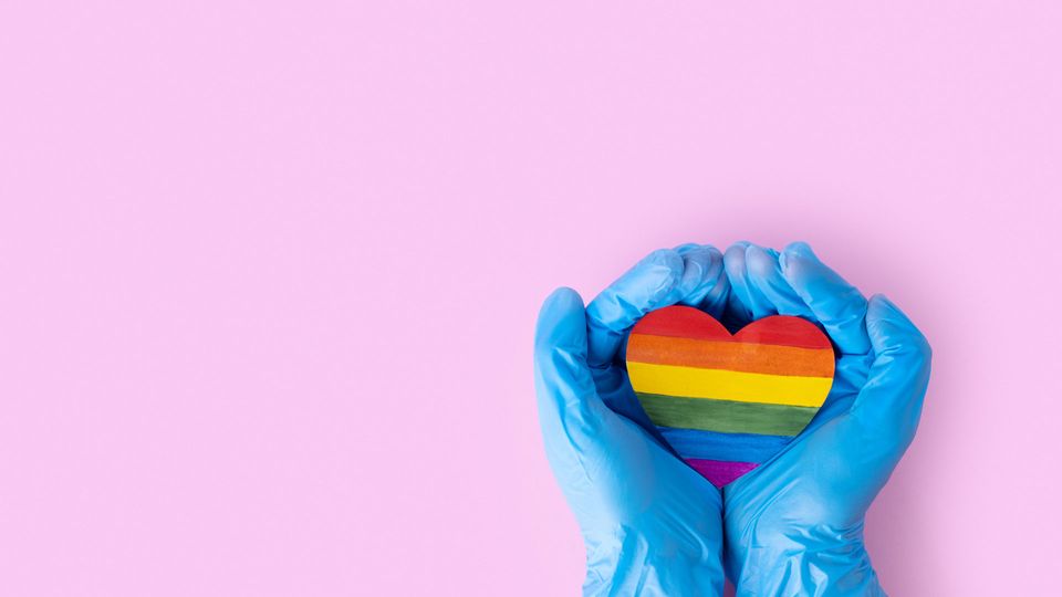 Rainbow heart representing LGBTQ+ held by gloved hands.
