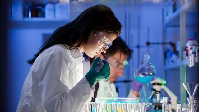 Scientist in protective gear using a pipette for experiments in a laboratory with test tubes. 
