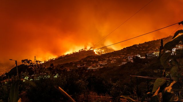 A wildfire burning through the distant hill, a Portuguese village closer to the camera, at risk from the flames. 