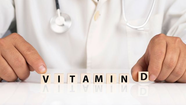 Doctor wearing a white coat and stethoscope lining up letter tiles to spell Vitamin D.  