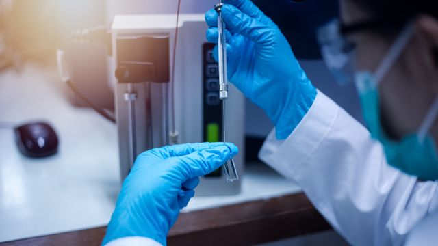Scientist wearing blue gloves preparing a sample for mass spectrometry analysis in a laboratory 