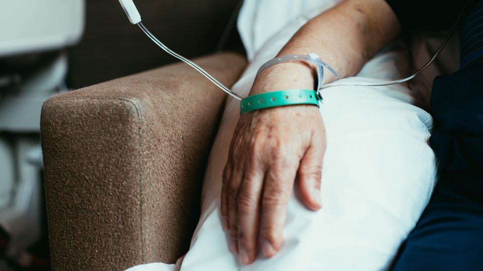 An older patient's hand on a pillow with medical bands and has a drip attached 