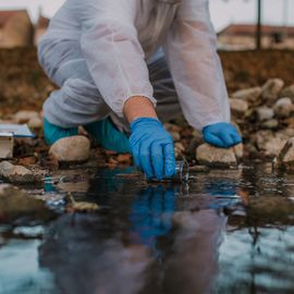 Scientist in protective gear collecting water sample from a stream to test for environmental pollutants. 