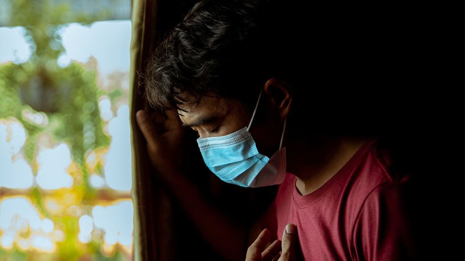 A man in a mask suffering from COVID-19 holding his chest.