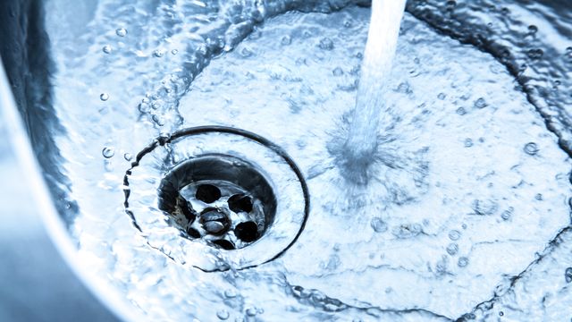 Metal sink, plug-hole visible, tap running. 